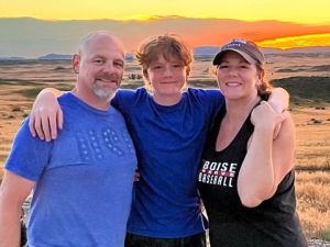 Three people standing in front of sunset and smiling.